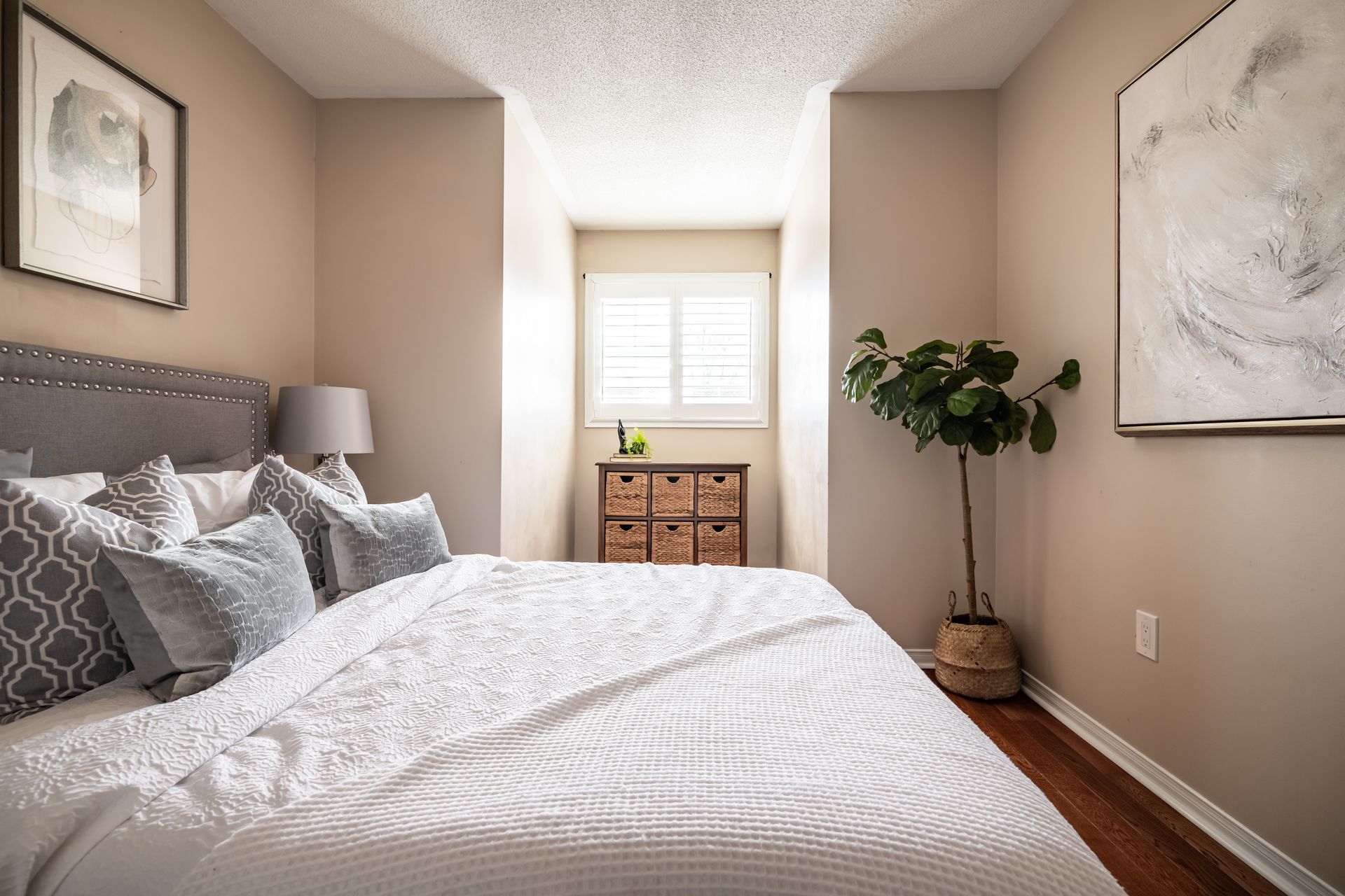A bedroom with a bed , dresser , lamp and a potted plant.