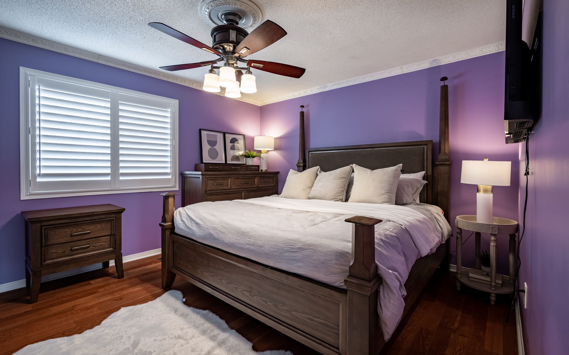 A bedroom with purple walls , a bed , a nightstand , and a ceiling fan.