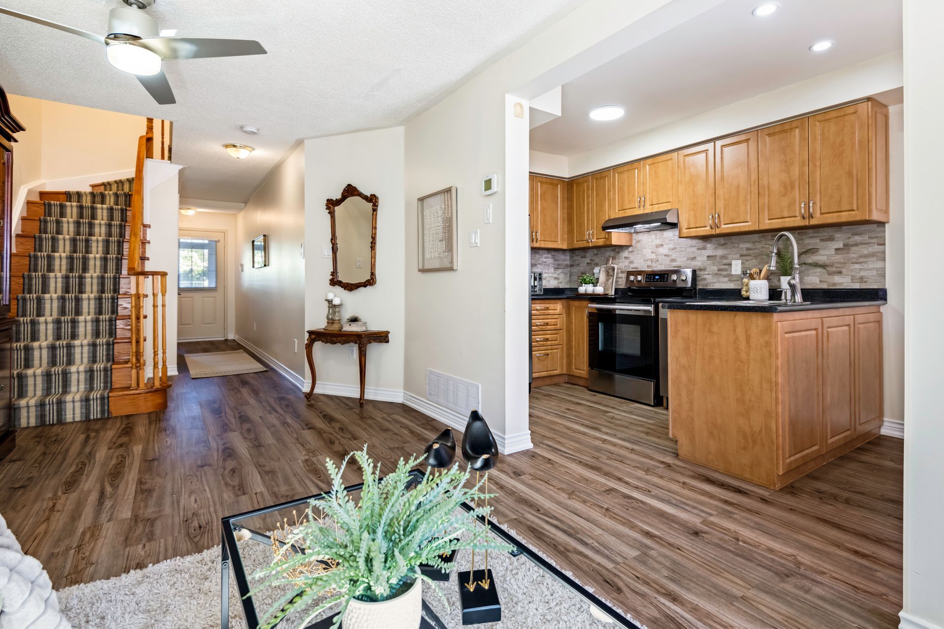 A living room and kitchen in a house with hardwood floors and a ceiling fan.