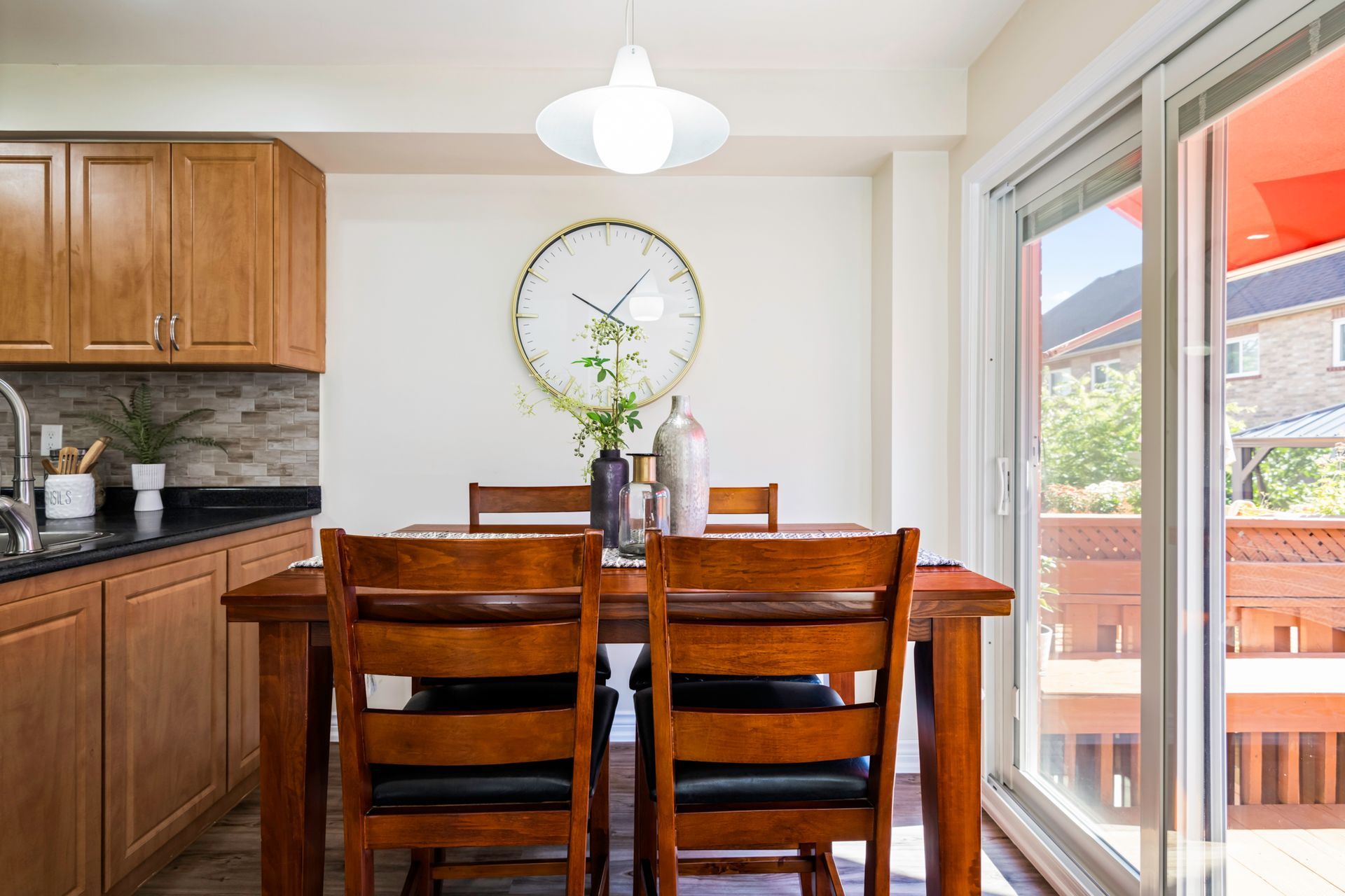 A dining room table and chairs in a kitchen with a clock on the wall.
