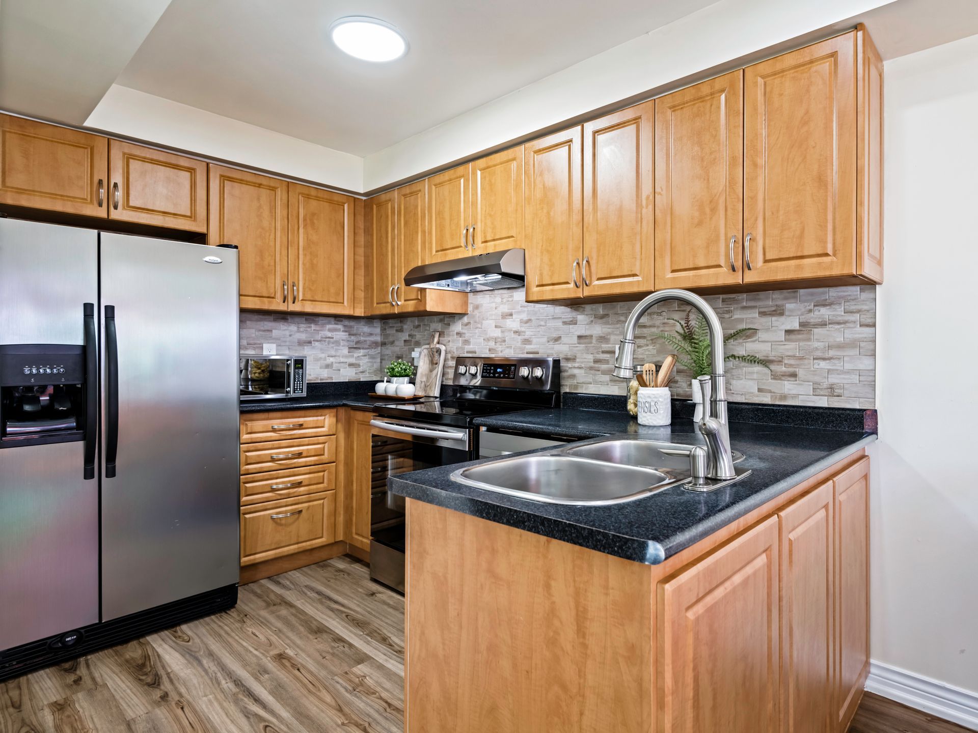 A kitchen with wooden cabinets , stainless steel appliances , a sink , and a refrigerator.