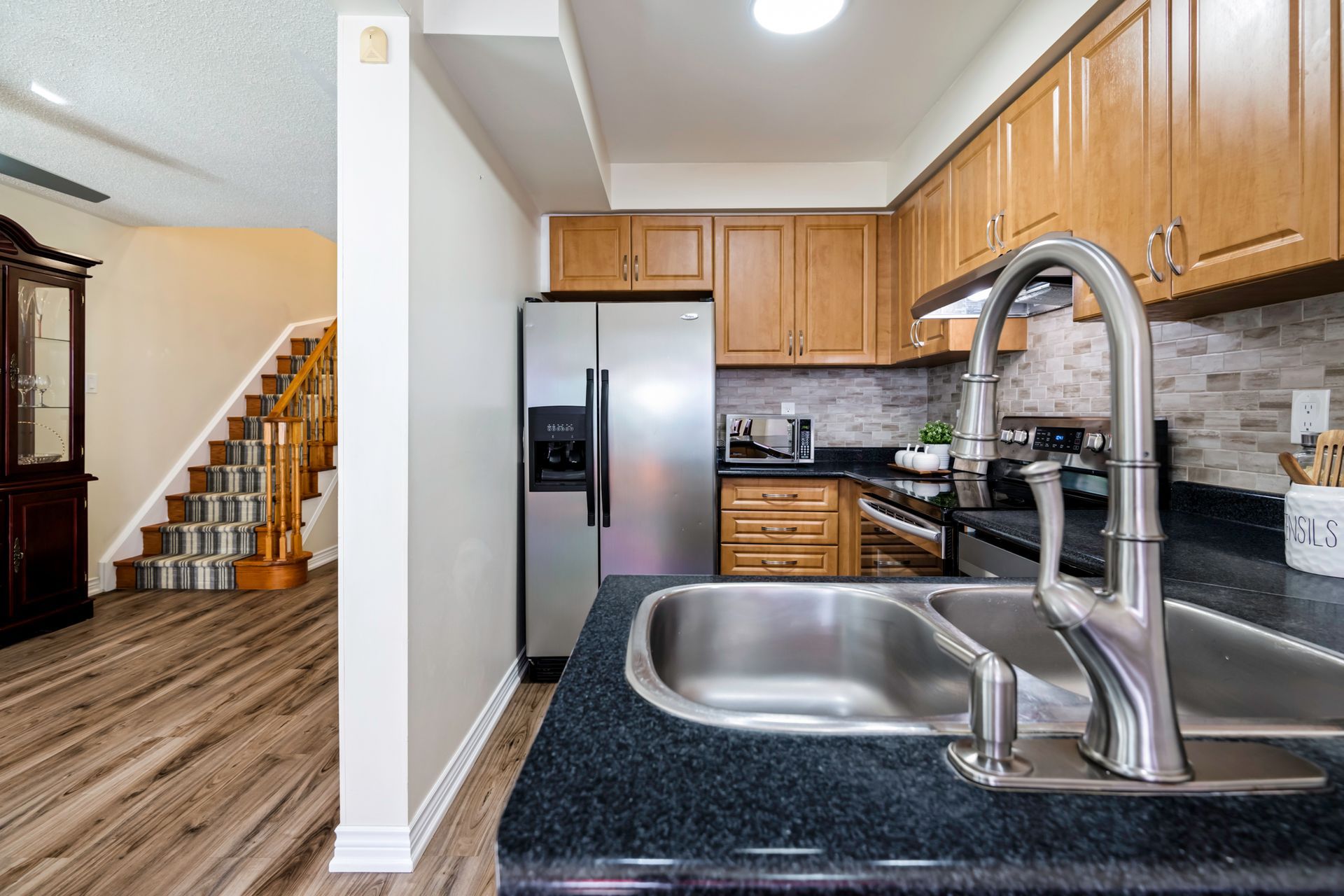 A kitchen with a sink , refrigerator , stove and stairs.