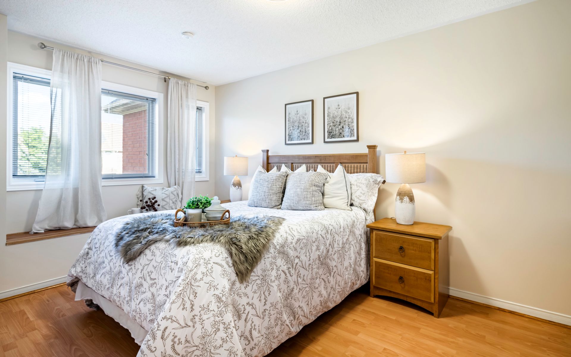 A bedroom with a large bed , nightstand , lamps and two windows.