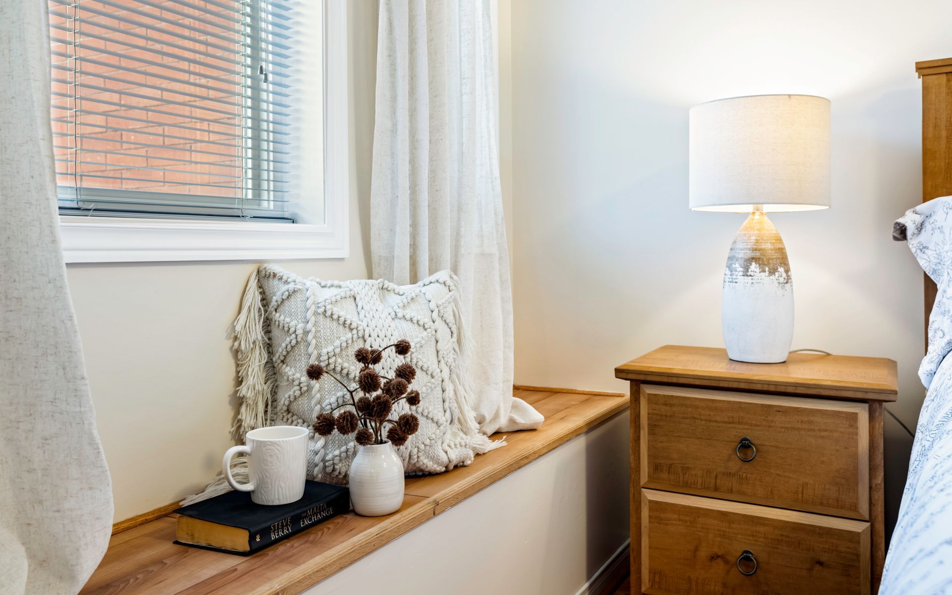 A bedroom with a window seat , nightstand and lamp.