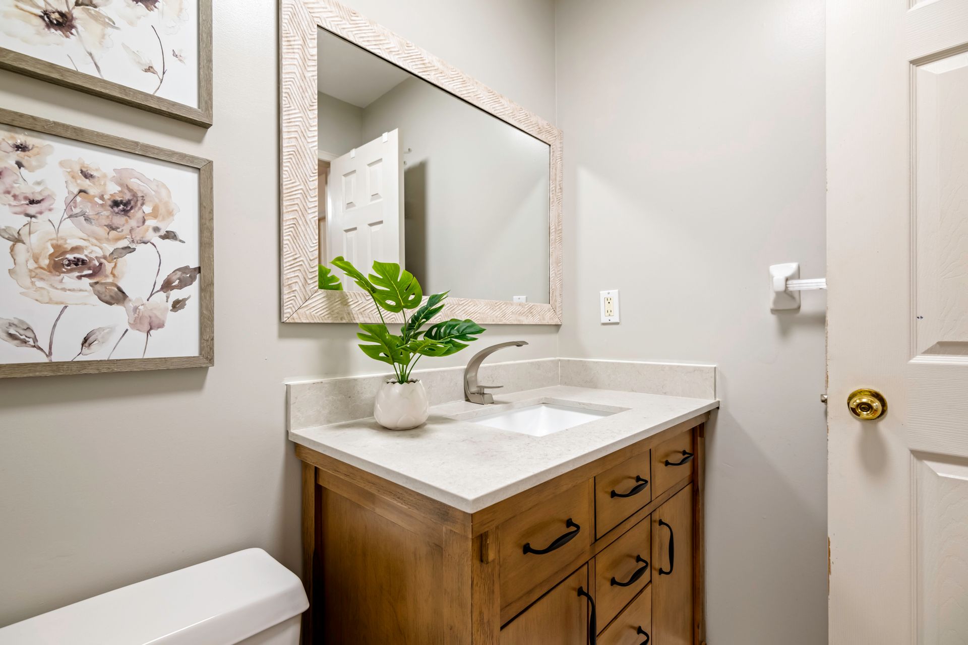 A bathroom with a sink , toilet , mirror and paintings on the wall.
