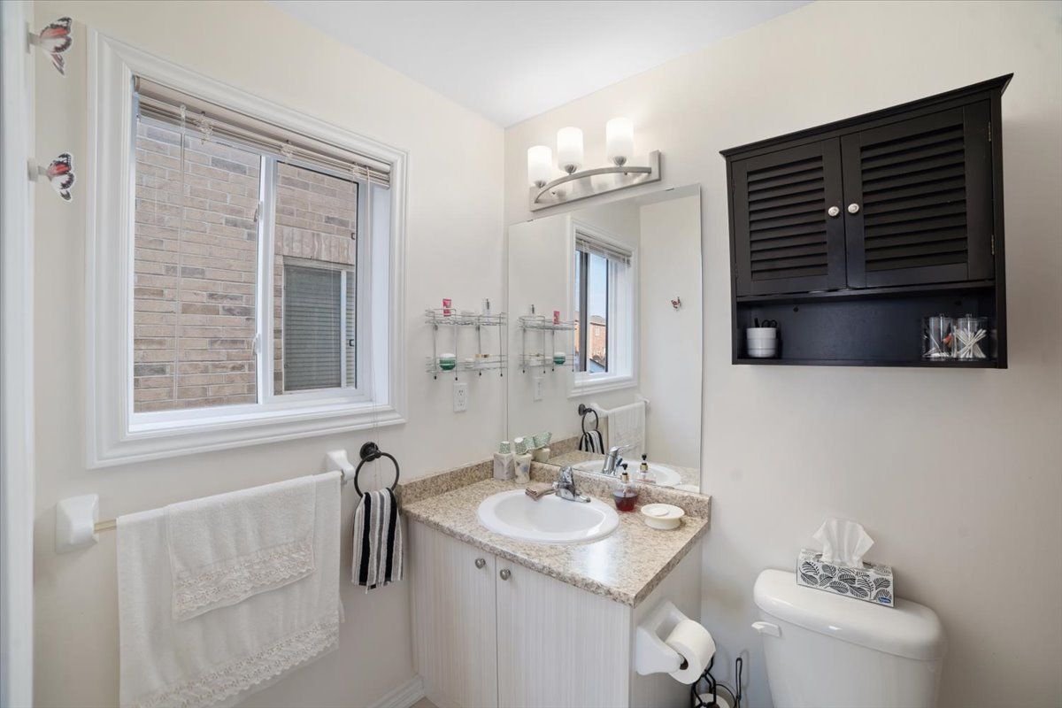 A bathroom with a sink , toilet , mirror and window.