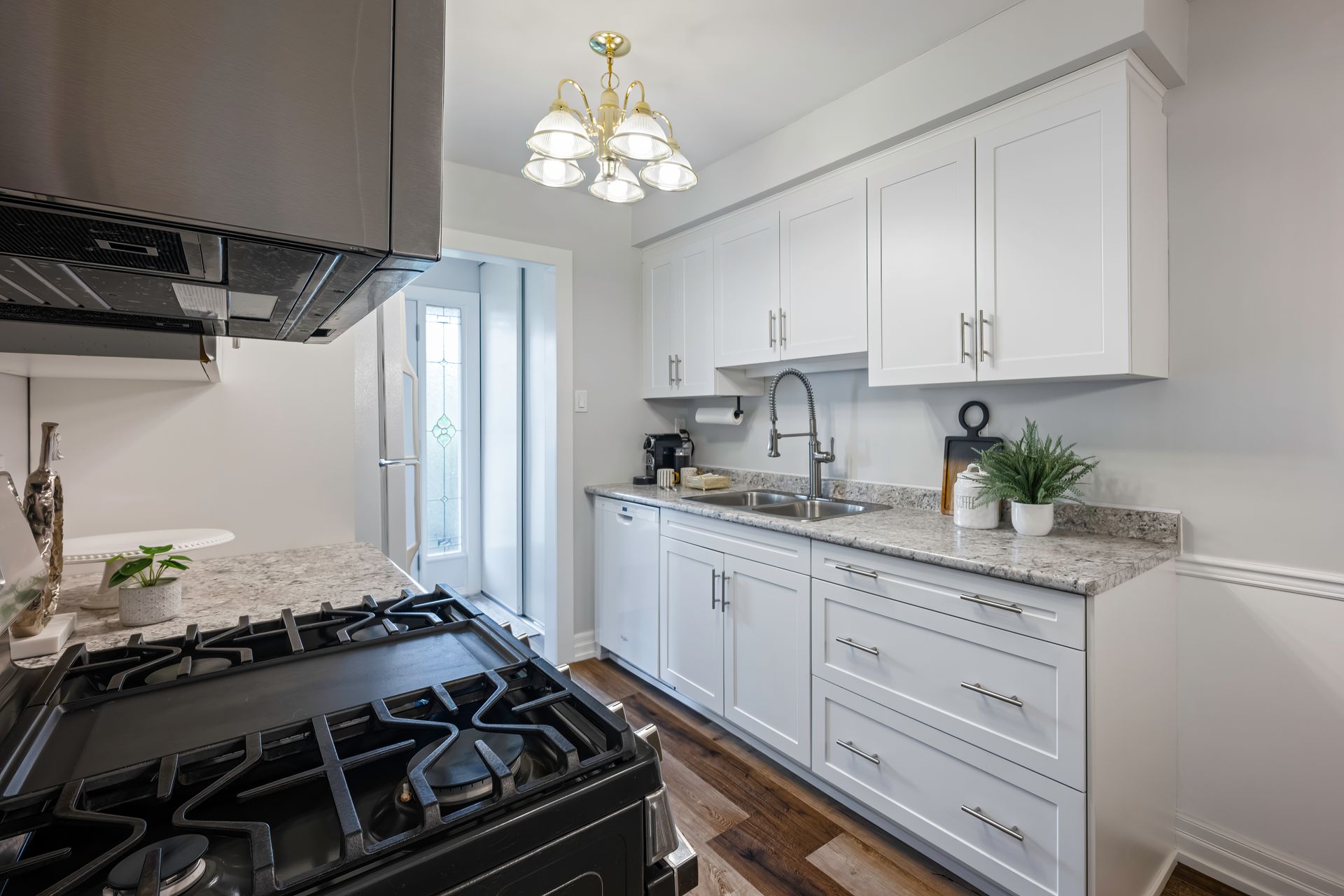 A kitchen with white cabinets , stainless steel appliances , a stove and a sink.