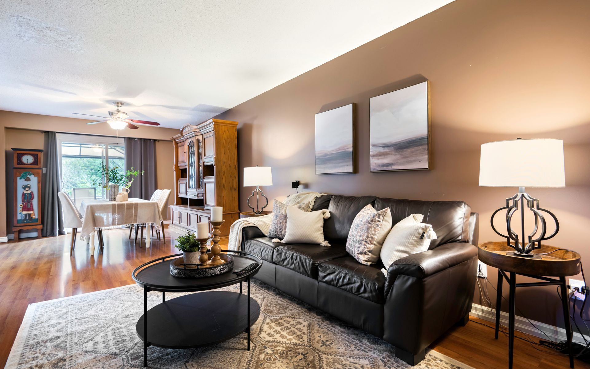 A living room with a couch , coffee table , lamps and a dining room in the background.