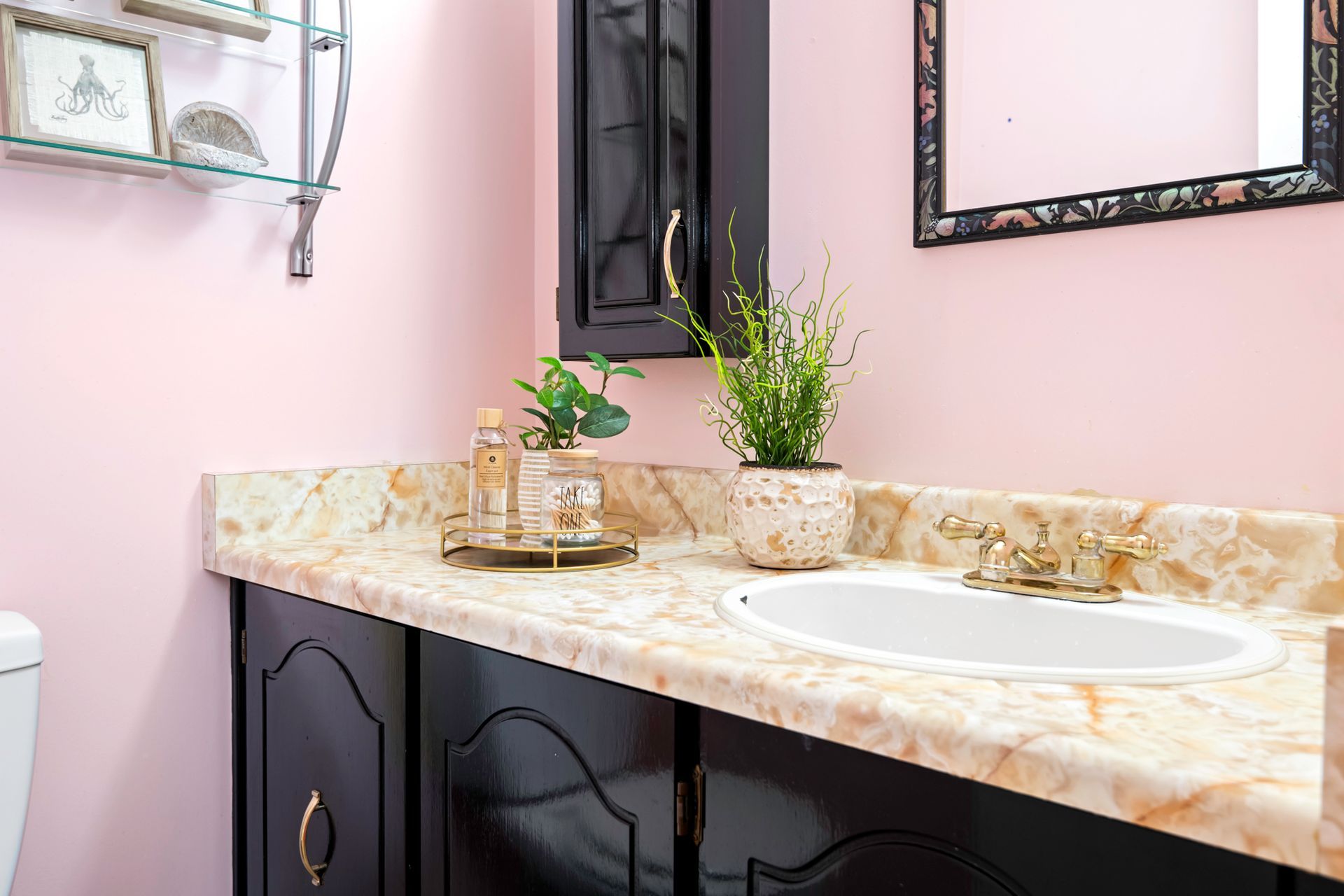 A bathroom with pink walls , black cabinets , a sink and a mirror.