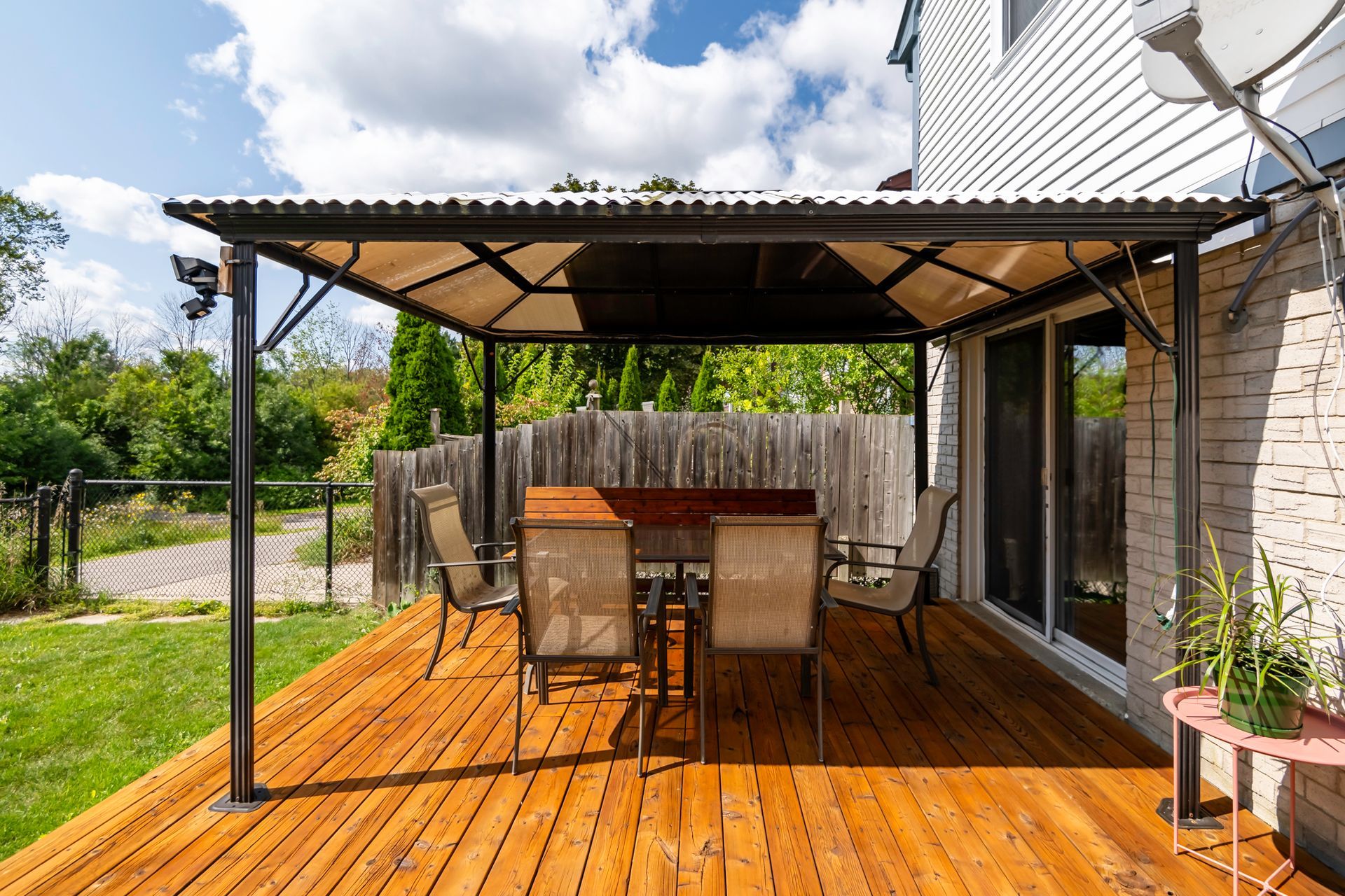 A wooden deck with a table and chairs under a canopy.