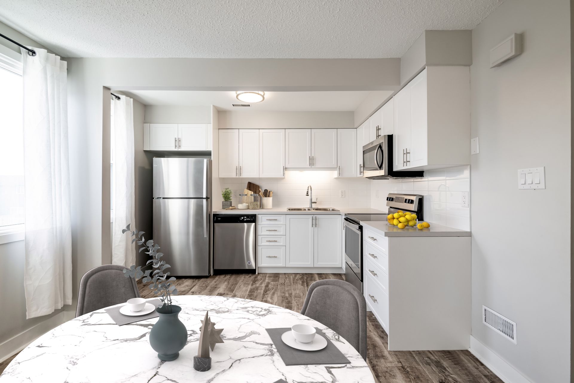 A kitchen with white cabinets and stainless steel appliances and a dining table.