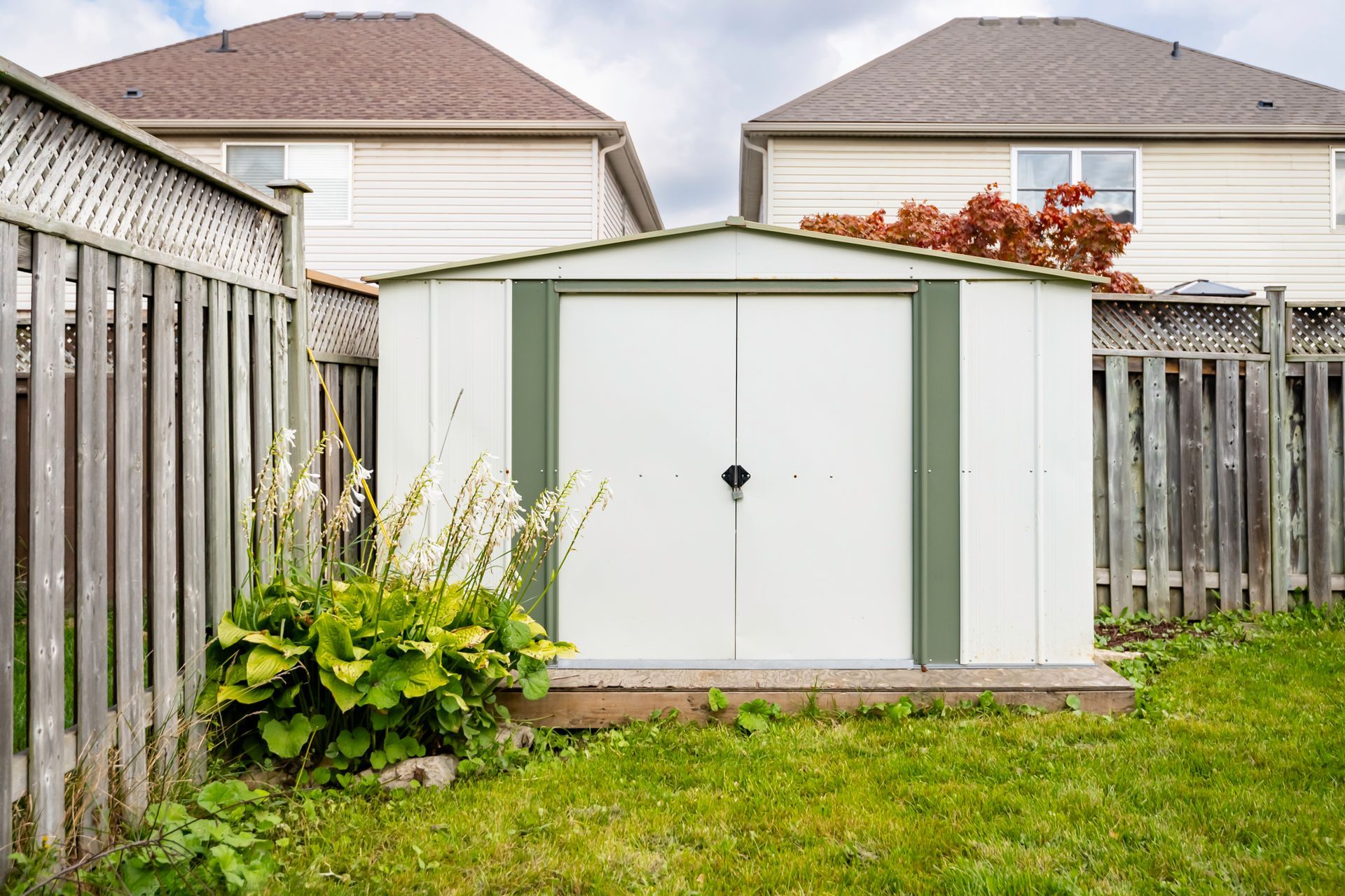 A white shed with green trim is in the backyard next to a wooden fence.