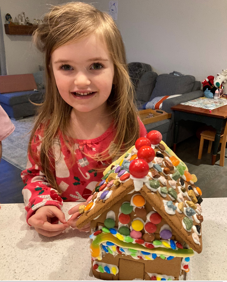 A little girl is holding a gingerbread house on a counter.