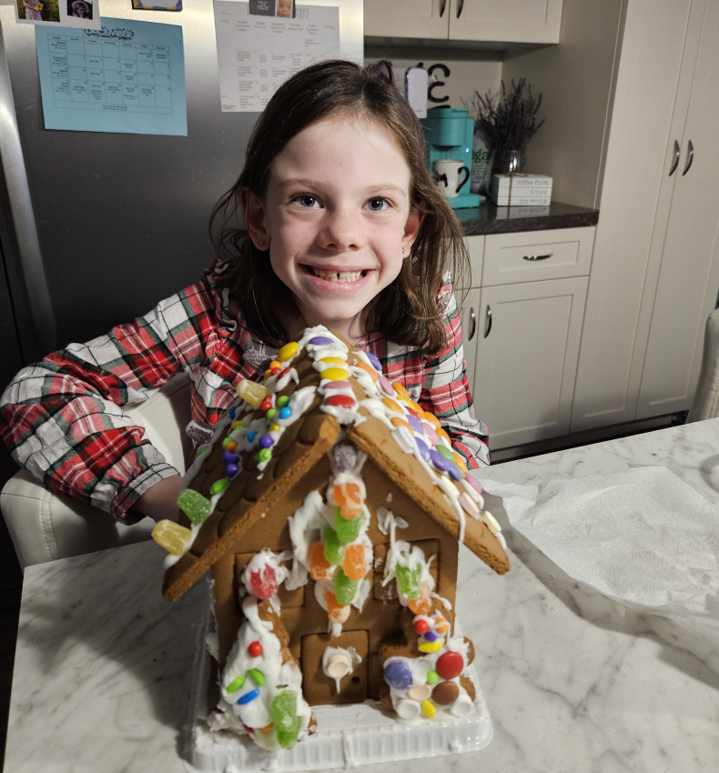 A little girl is sitting at a table with a gingerbread house on it