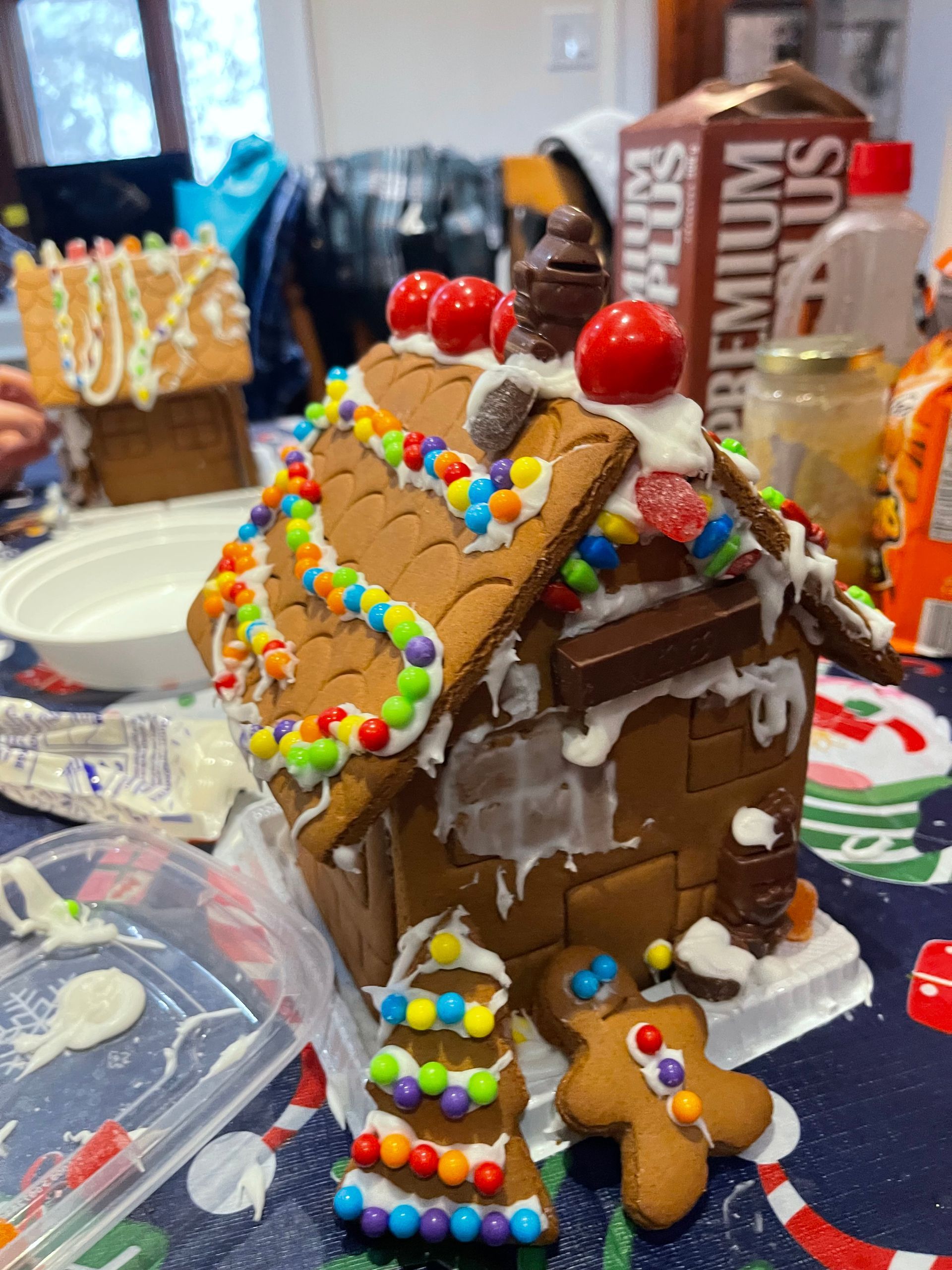 A gingerbread house is sitting on a table next to a box of premium plus.