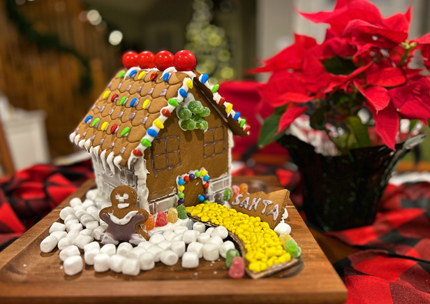 A gingerbread house is sitting on a wooden cutting board next to a potted plant.