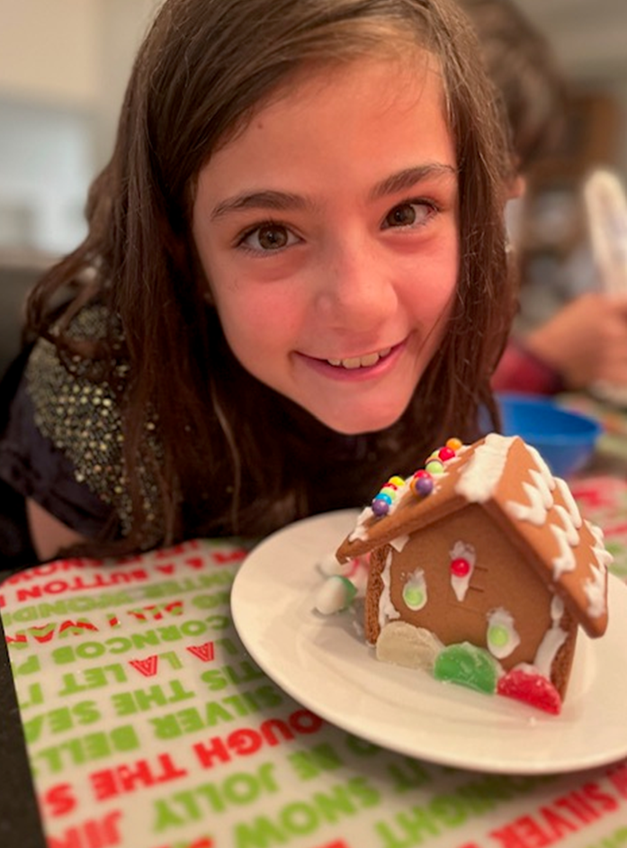 A little girl is holding a gingerbread house on a plate.