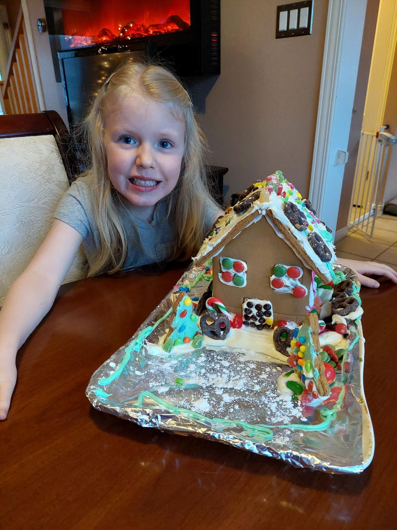 A little girl is sitting at a table with a gingerbread house on it.