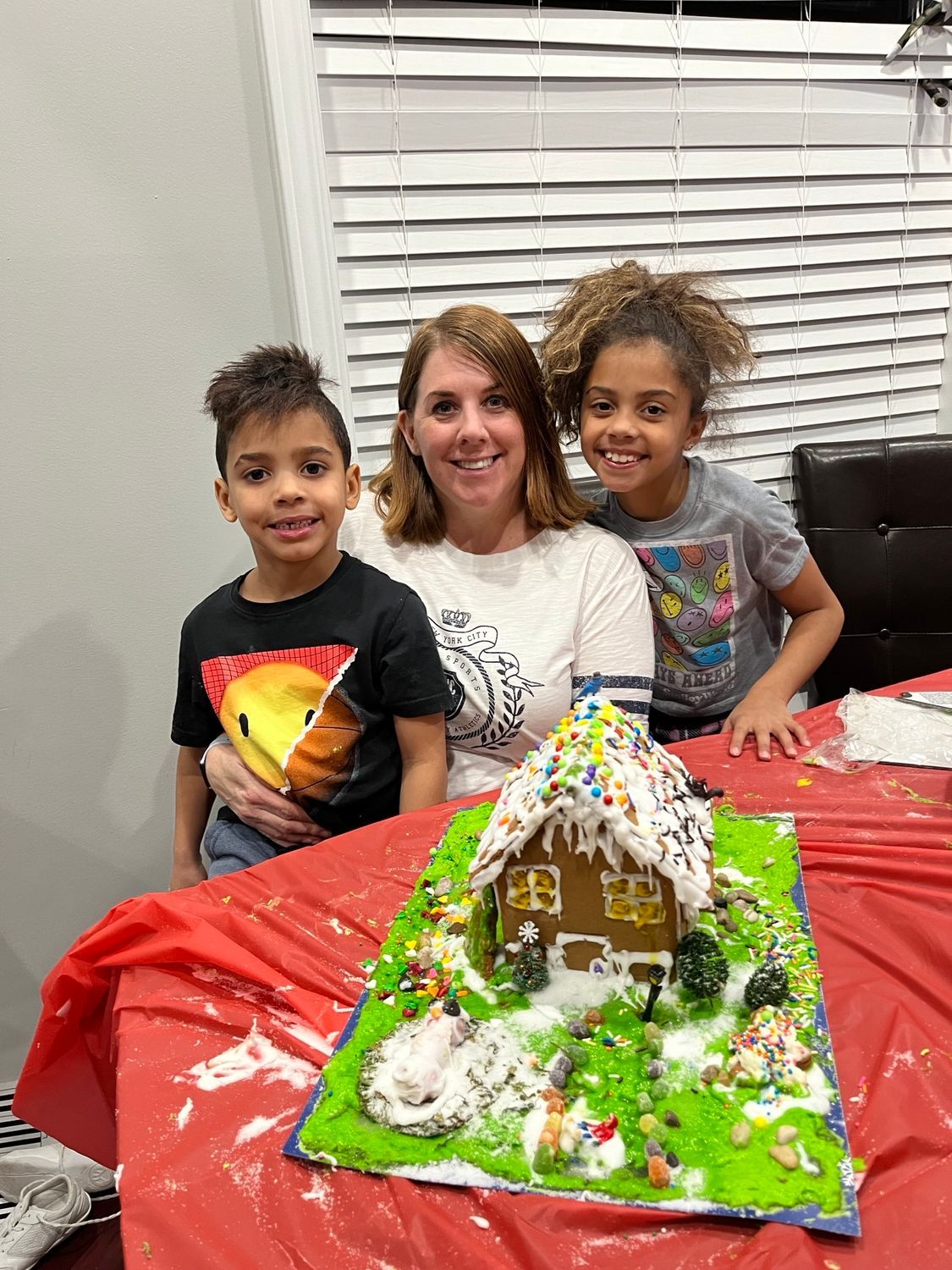 A woman and two children are sitting at a table with a gingerbread house.