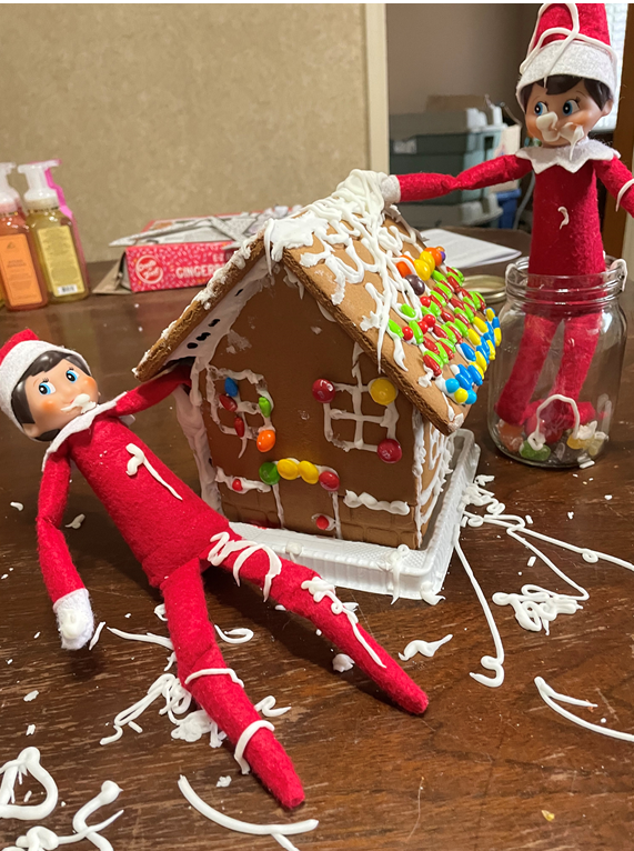Two elf on the shelf are decorating a gingerbread house