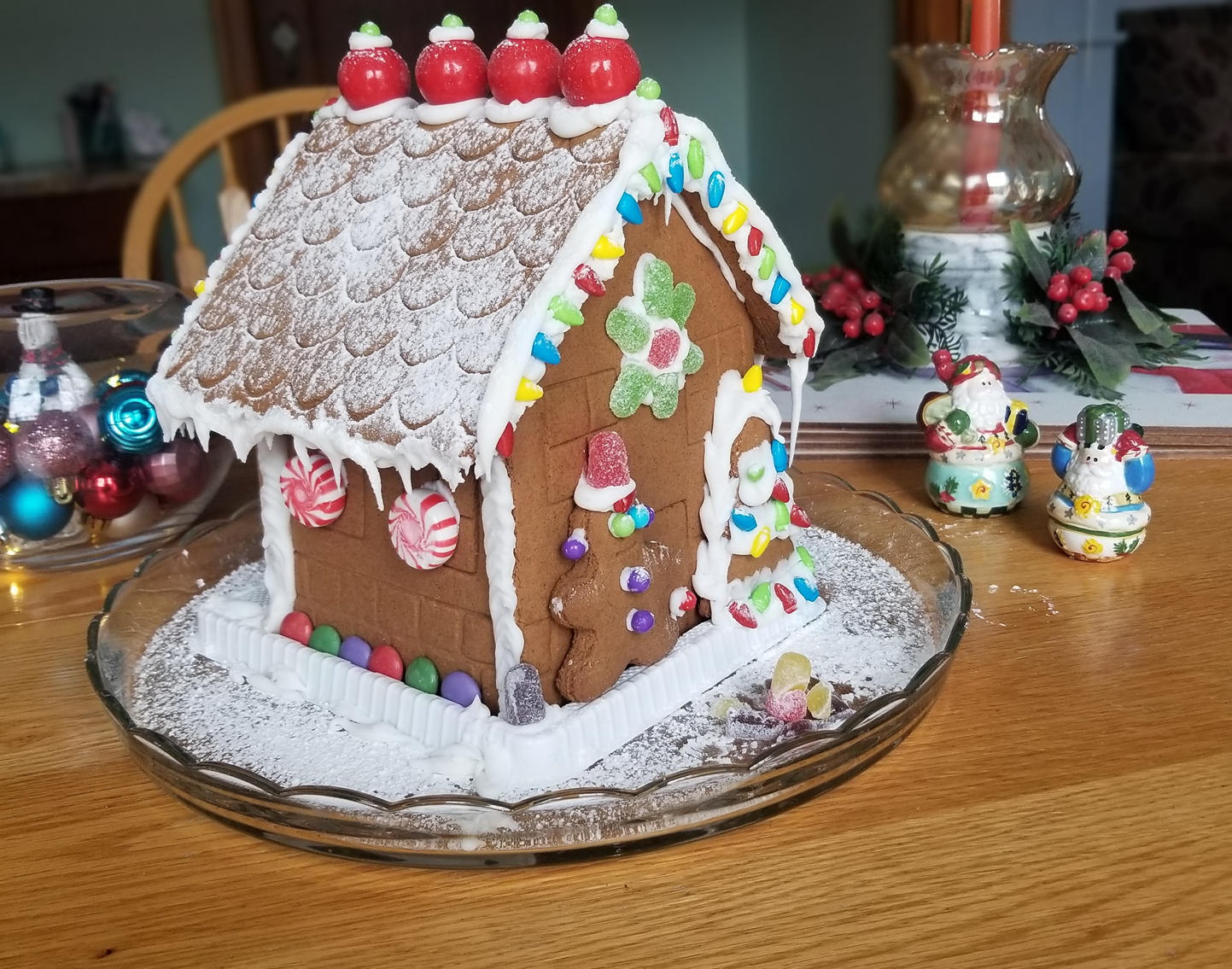 A gingerbread house is sitting on a glass plate on a table.