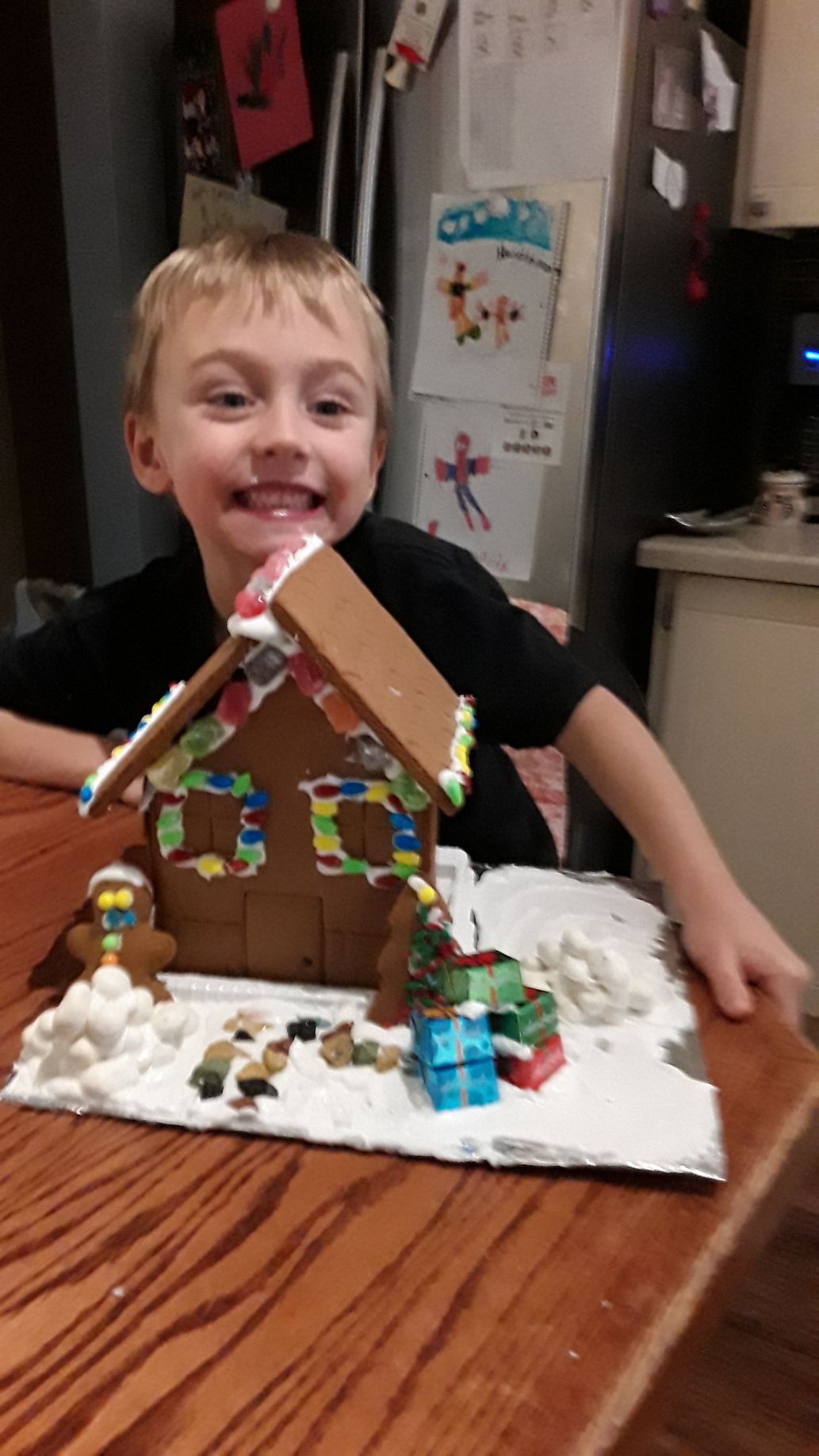 A young boy is sitting at a table with a gingerbread house on it.