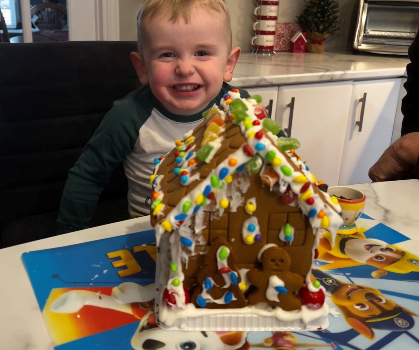 A little boy is sitting at a table with a gingerbread house on it