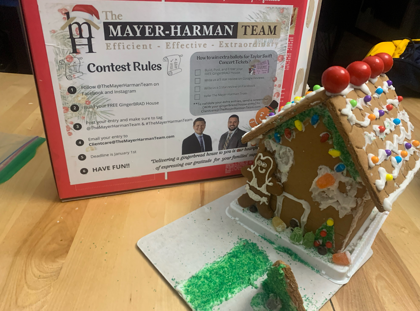 A gingerbread house is sitting on a table next to a box that says mayer-harman team contest rules