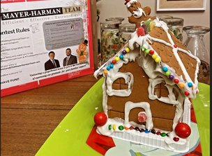 A gingerbread house sits on a table next to a mayer-harman team certificate