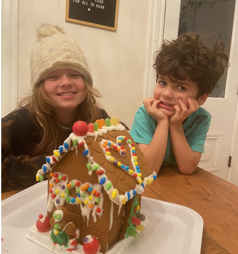 A boy and a girl sitting next to a gingerbread house