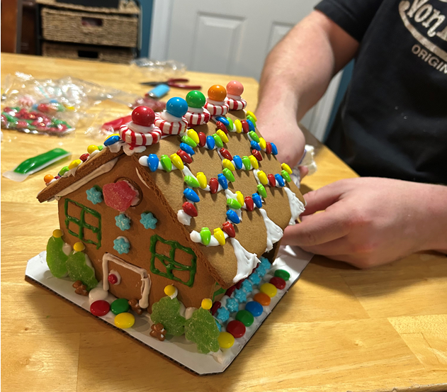 A person is decorating a gingerbread house on a wooden table