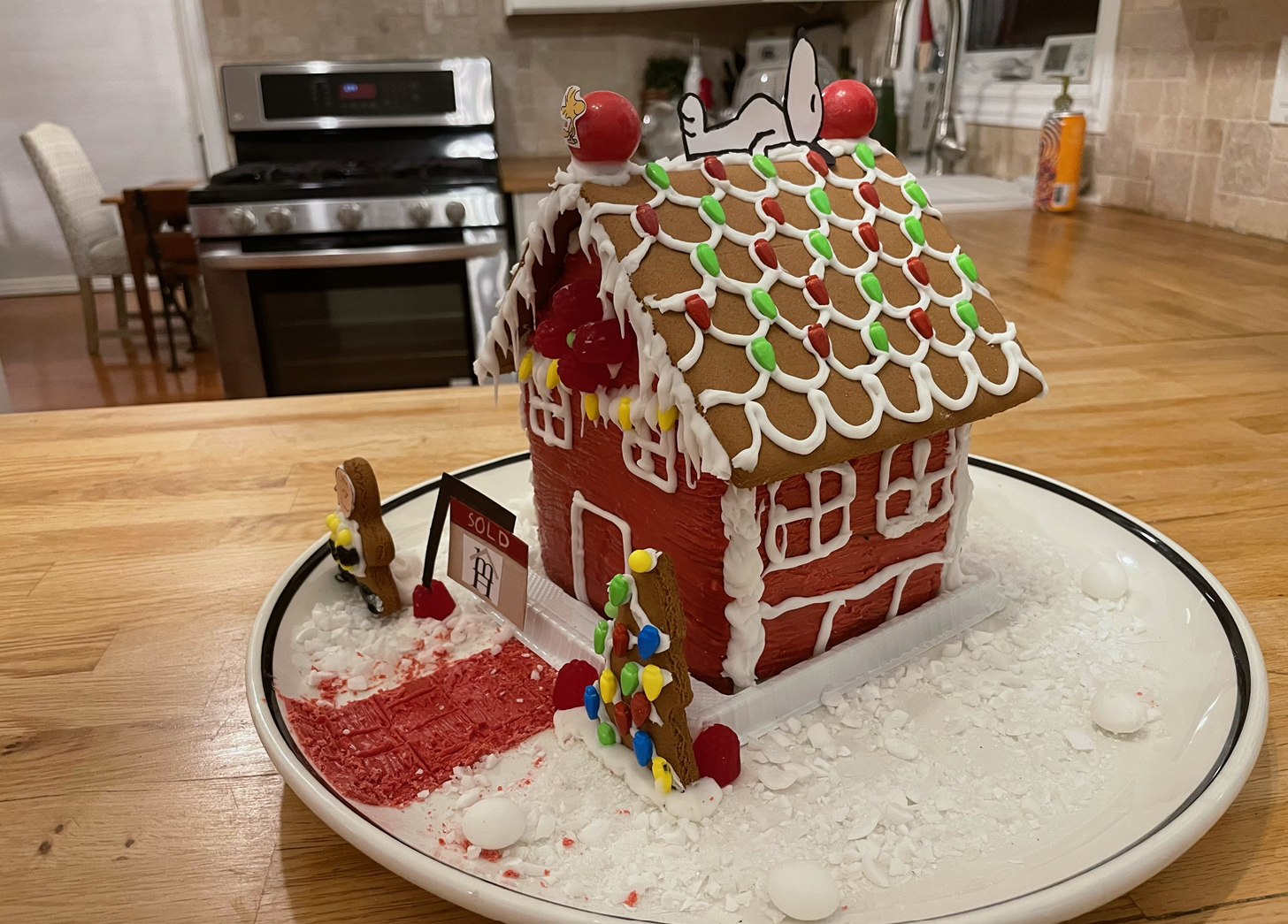 A gingerbread house is sitting on a white plate on a wooden table.