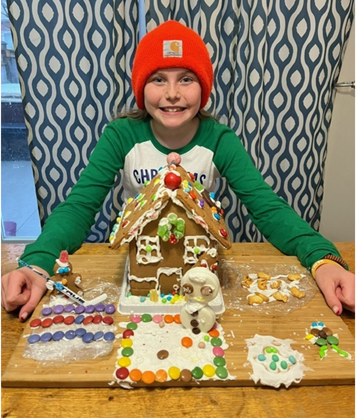 A young girl is sitting at a table with a gingerbread house on it.