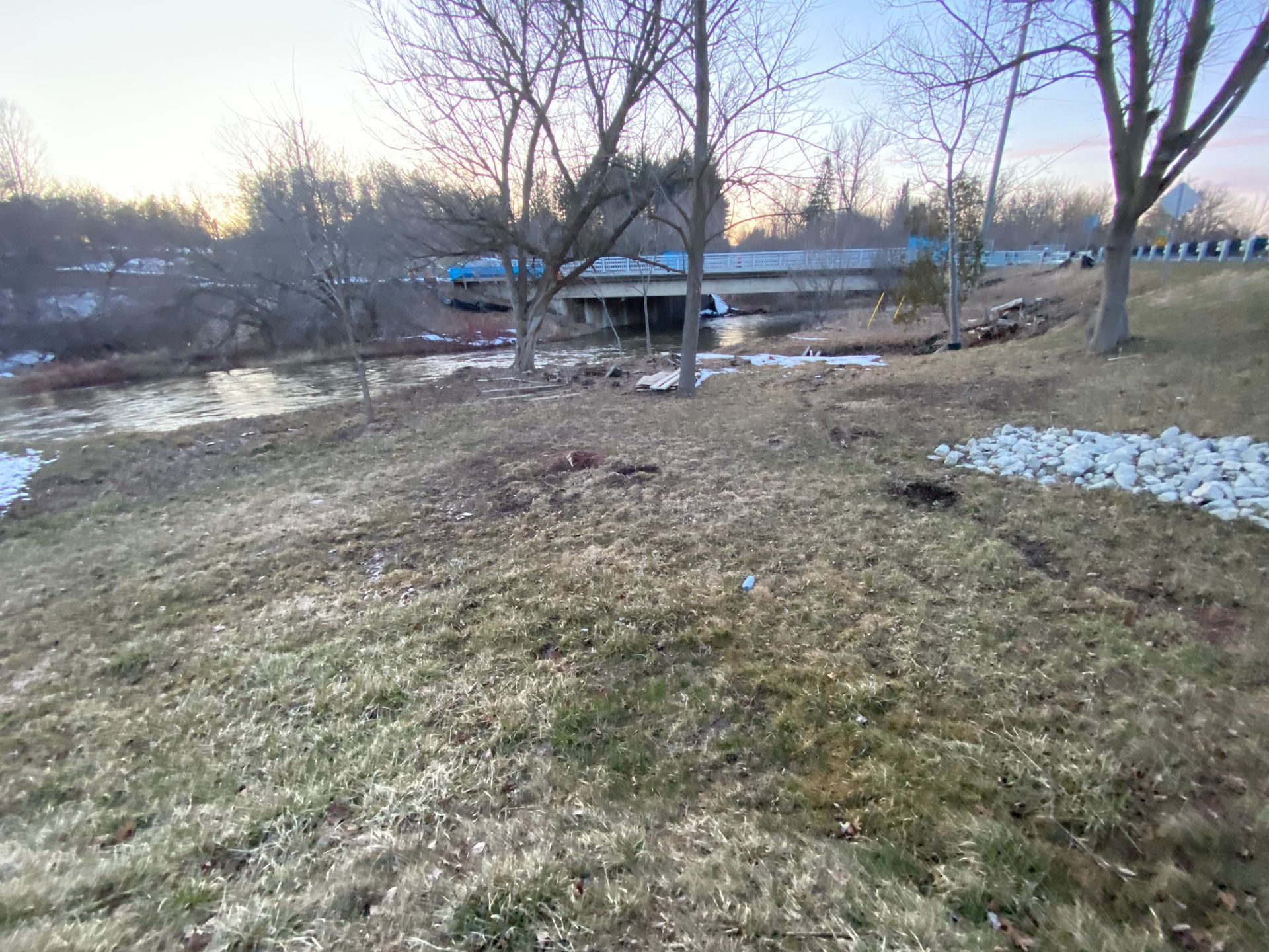A grassy hillside with trees and a bridge in the background.
