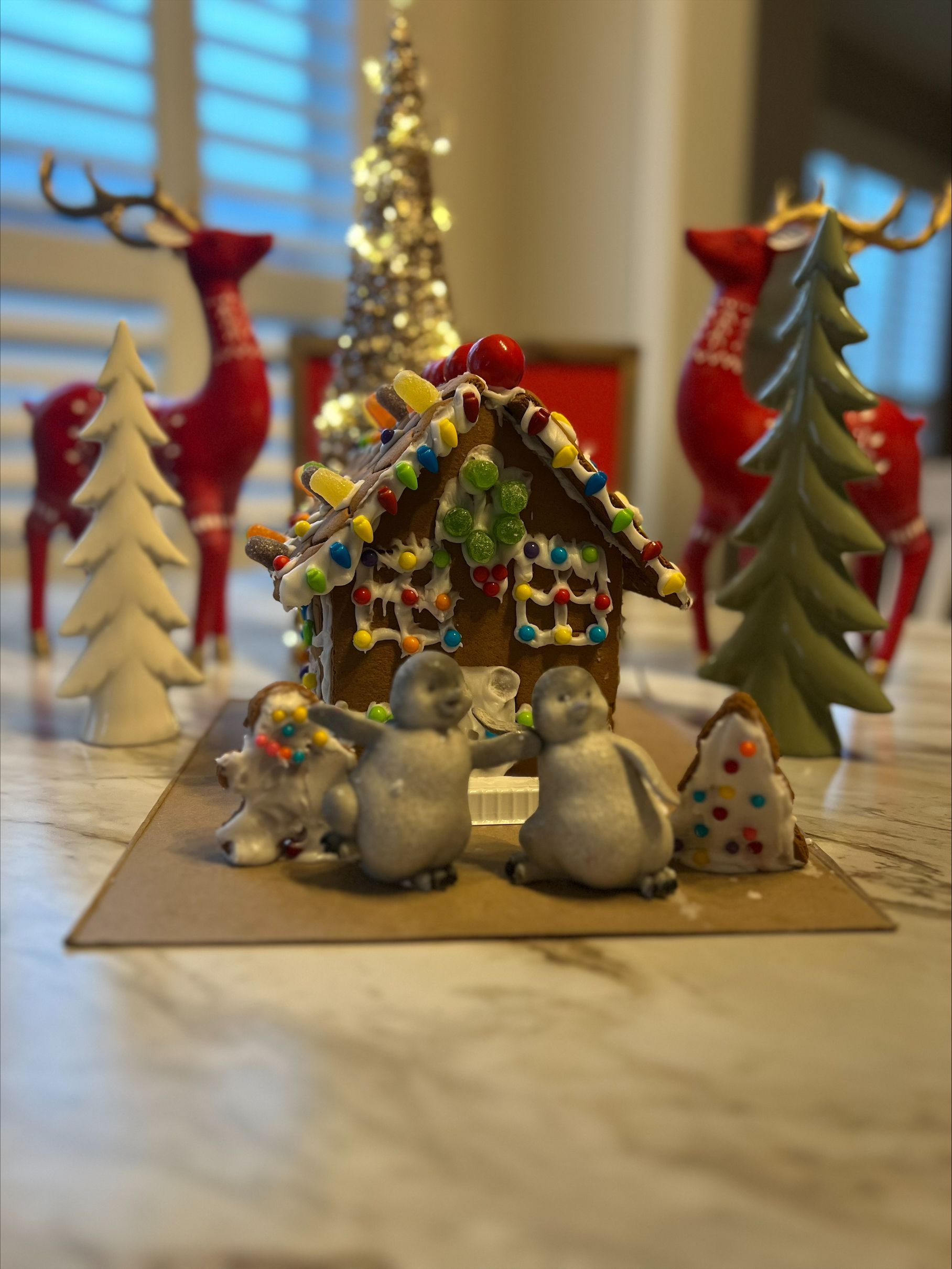 A gingerbread house with snowmen and a christmas tree in the background