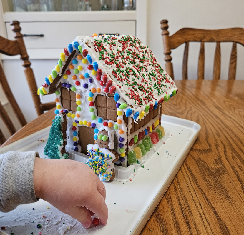 A child is decorating a gingerbread house with icing and sprinkles