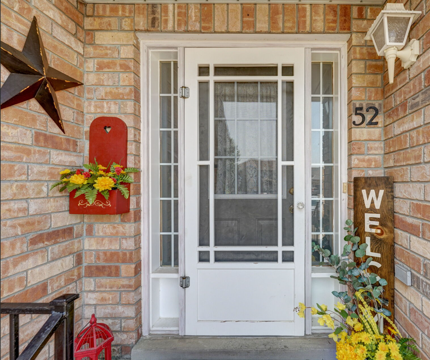 The front door of a brick house with a white screen door and a welcome sign.