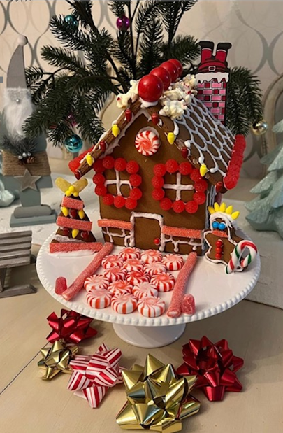 A gingerbread house is sitting on top of a cake stand next to a christmas tree.
