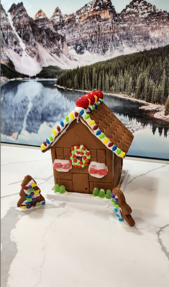 A gingerbread house is sitting on a counter next to a christmas tree.