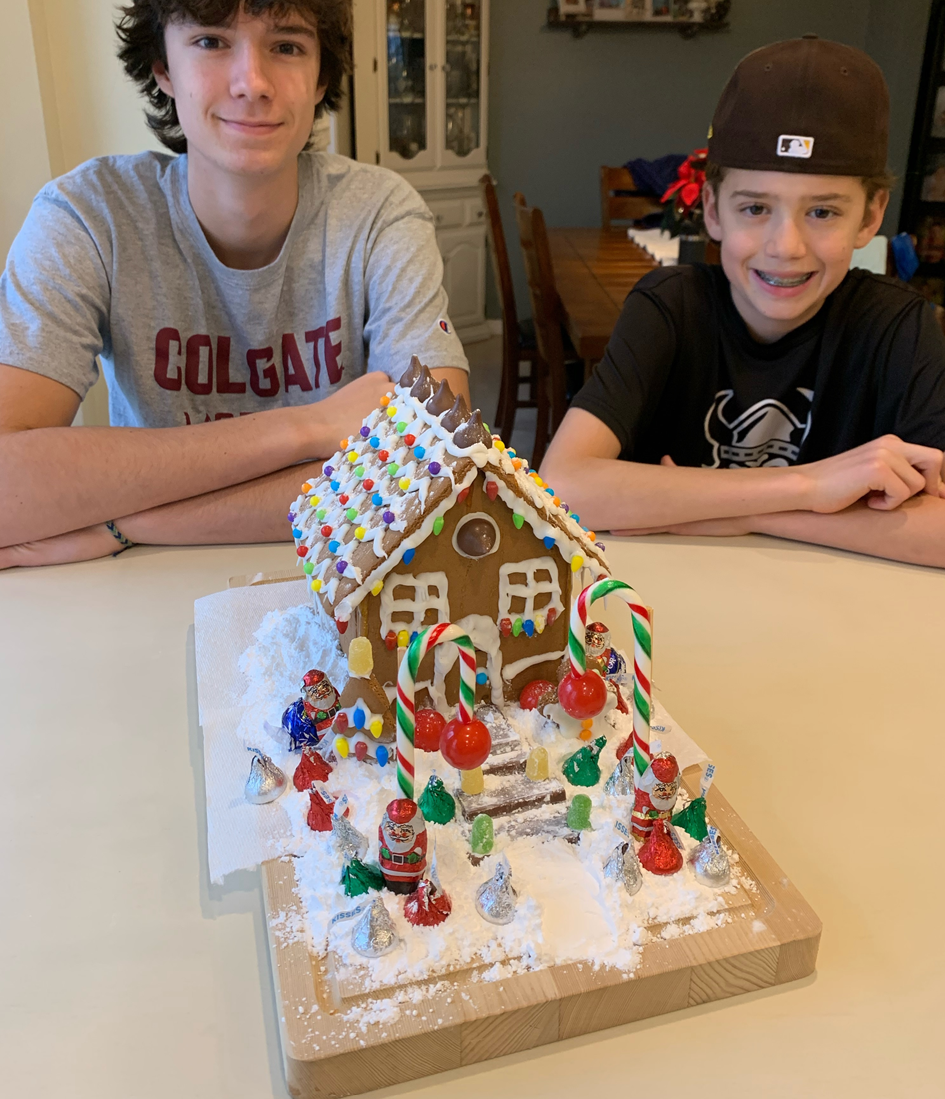 Two boys are sitting at a table with a gingerbread house on it.
