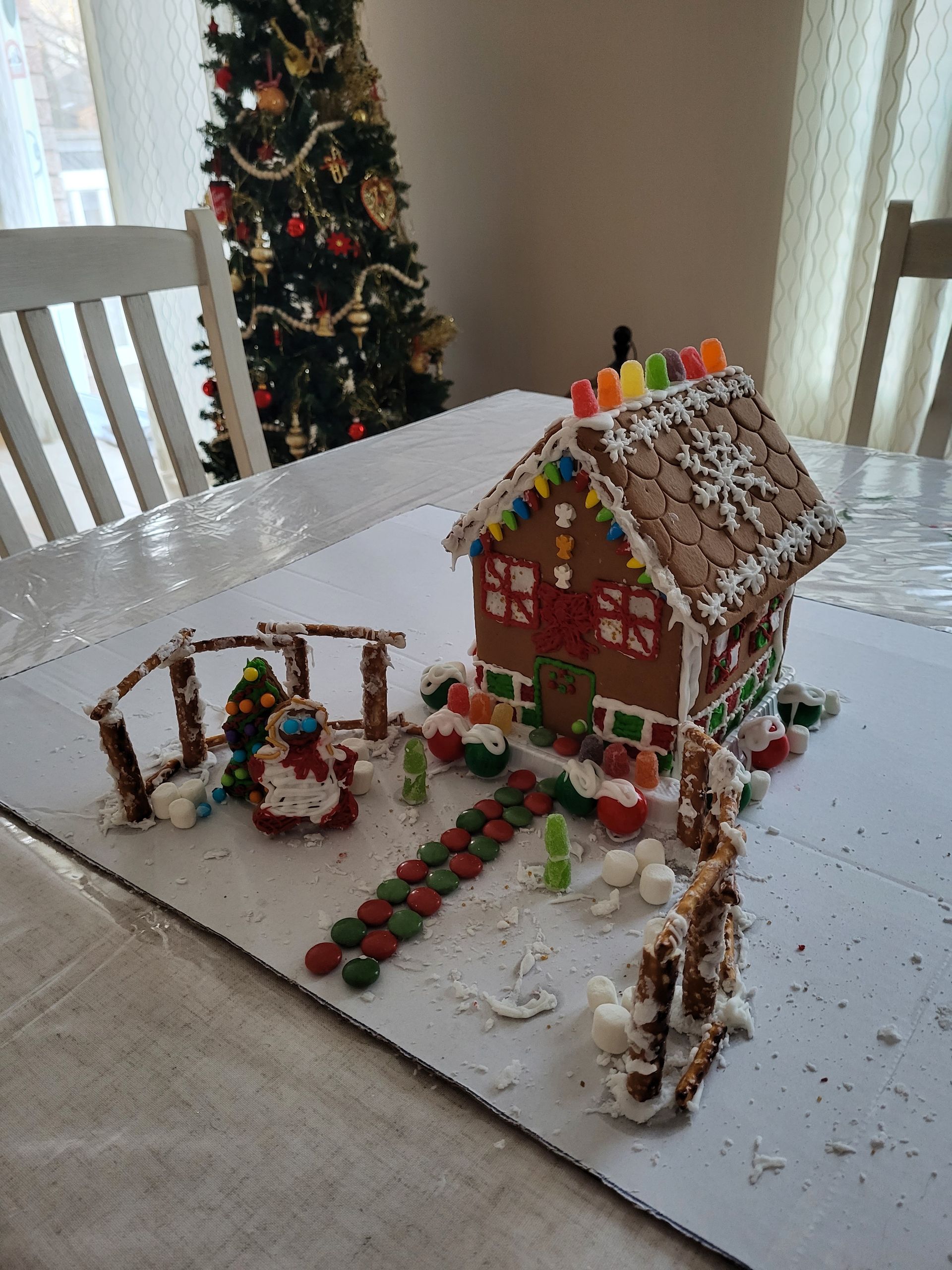 A gingerbread house is sitting on a table in front of a christmas tree.