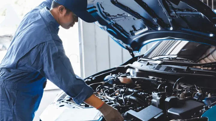 Mechanic in blue uniform inspecting a car engine bay.