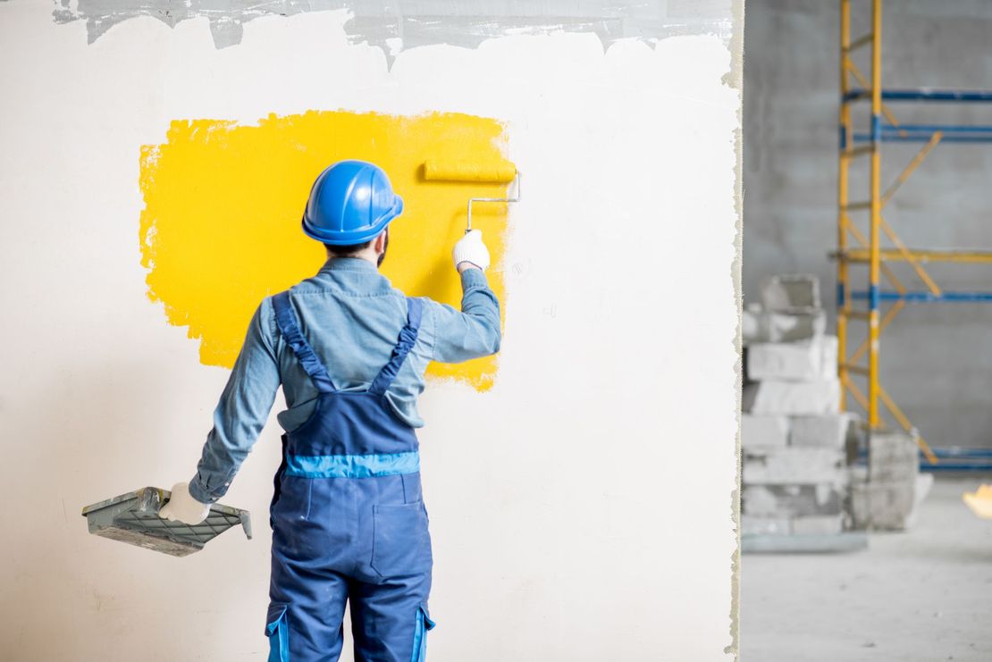 Un homme peint un mur en jaune avec un rouleau.