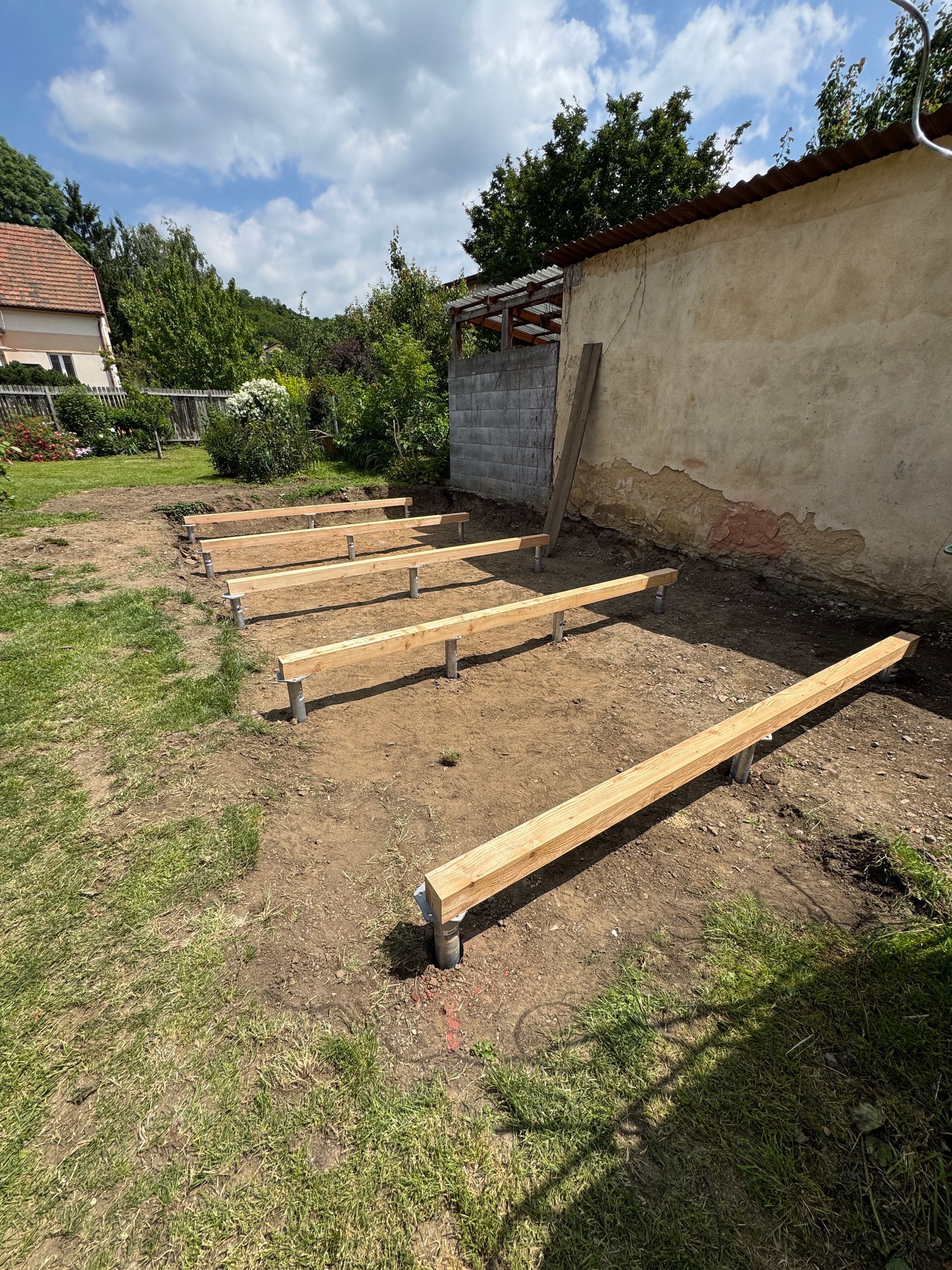 Wooden beams set on blocks in a yard, near a building. Construction in progress outdoors.
