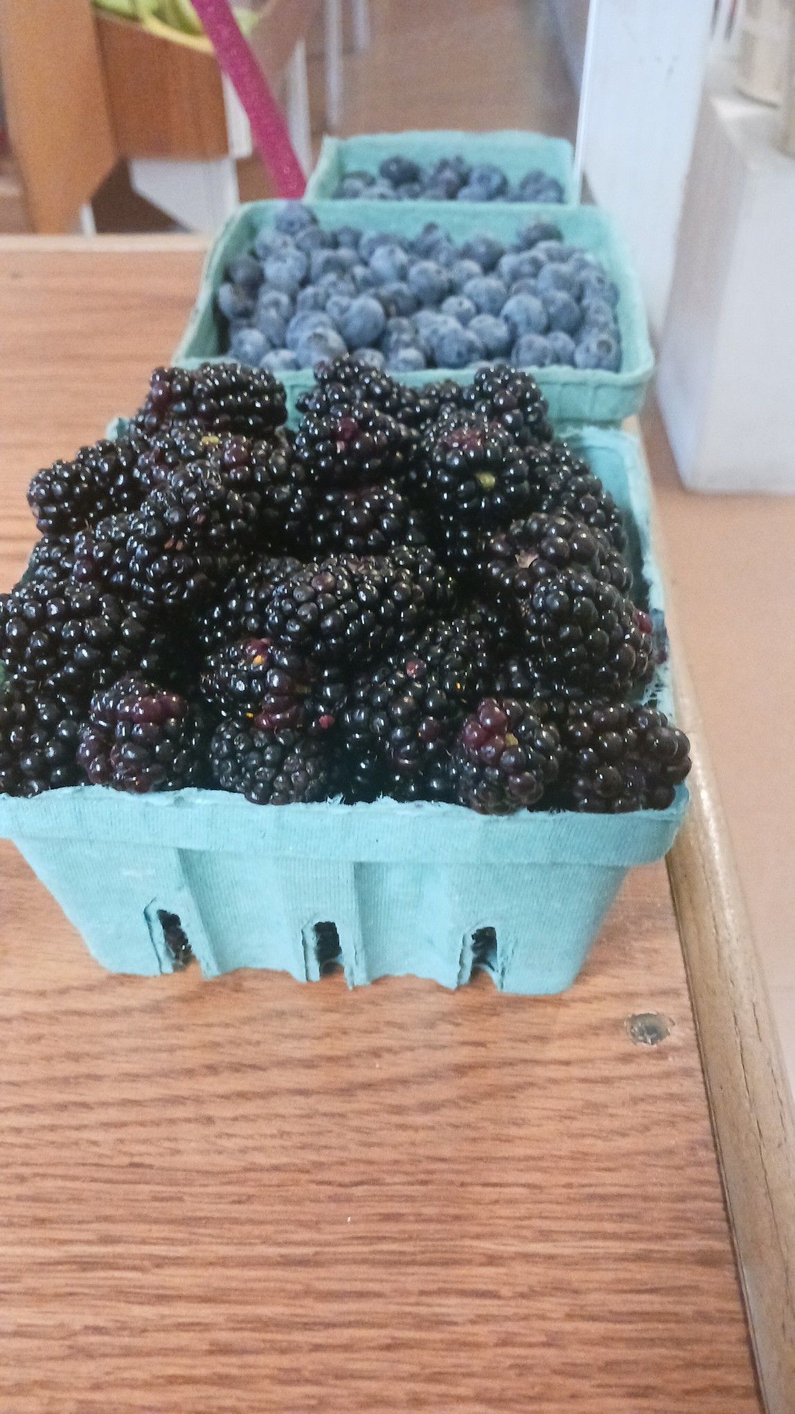 Blackberries and blueberries in green paper baskets on a wooden surface.