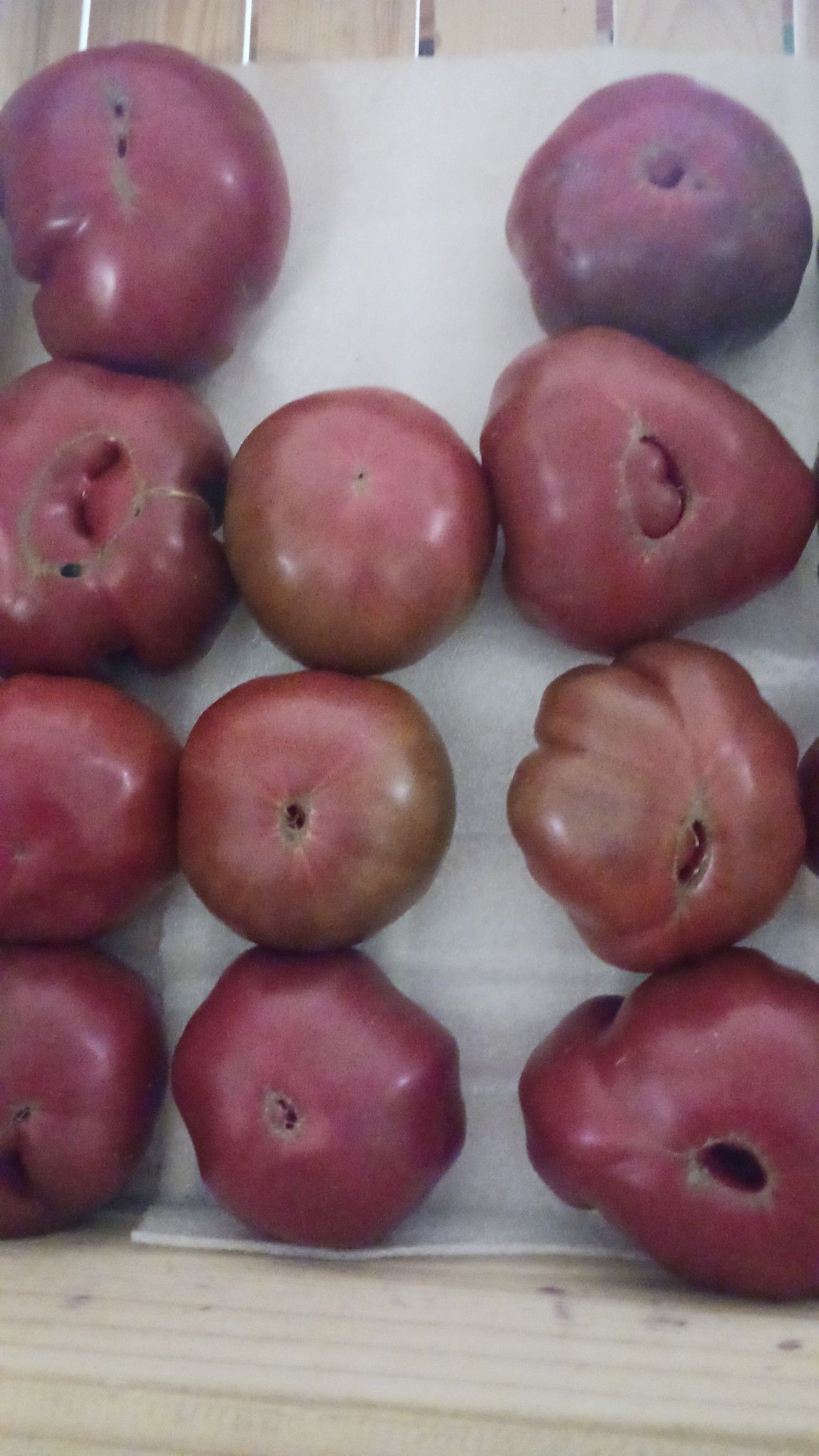 Dark red heirloom tomatoes in a wooden crate, some with imperfect shapes.