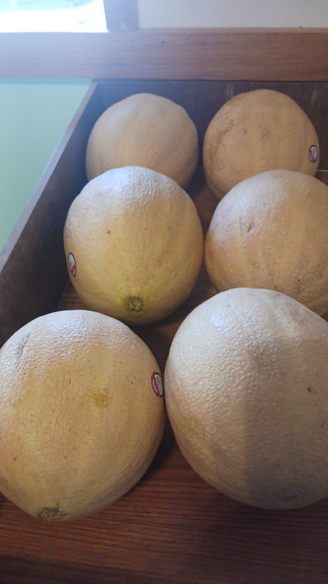 Six light-yellow citrus fruits, possibly grapefruits, in a wooden crate.