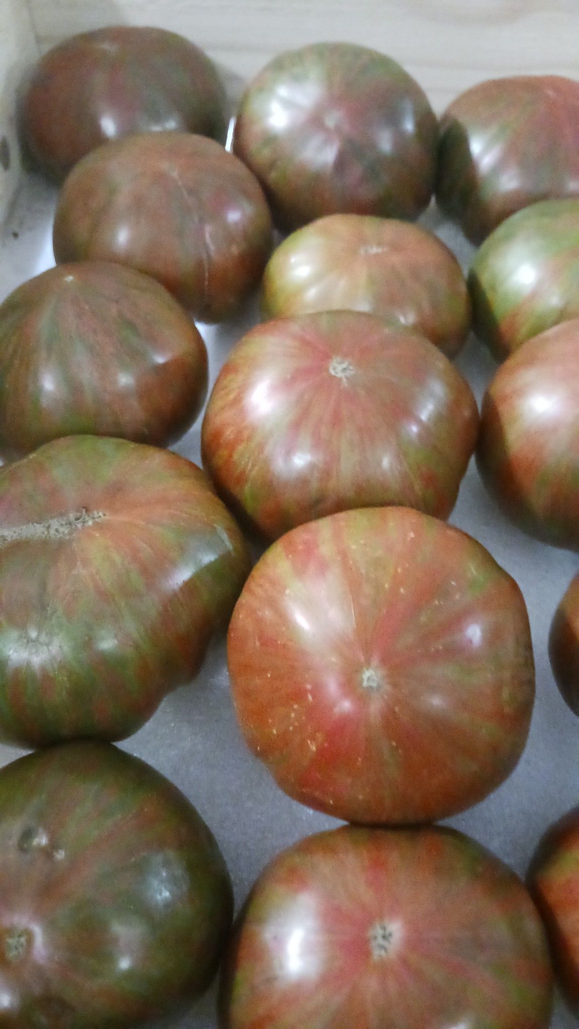 Dark-colored heirloom tomatoes, mostly brown and green, in a wooden crate.
