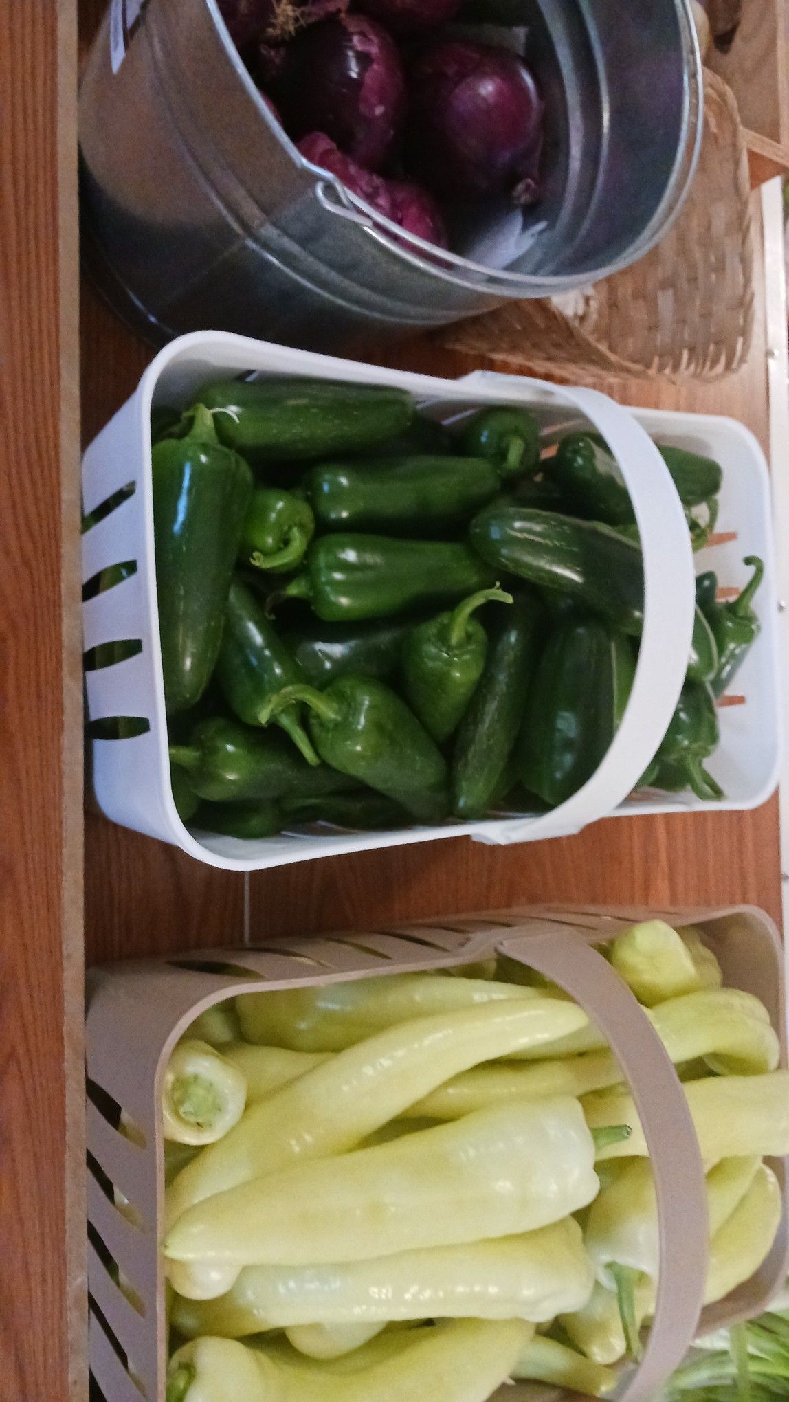 Three baskets of produce: red onions, jalapeño peppers, and banana peppers.