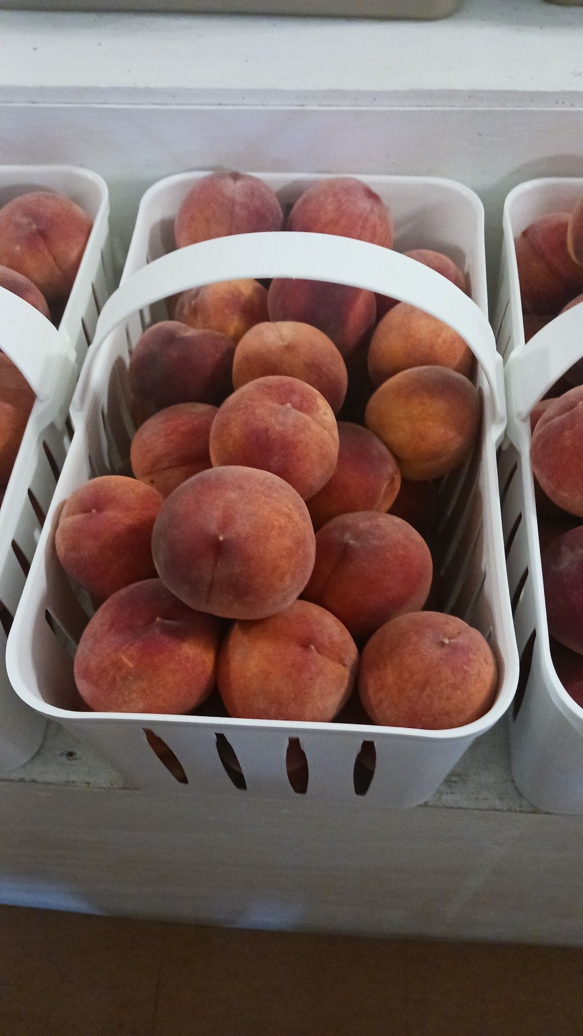 Peaches in white baskets, displayed at a market or store.